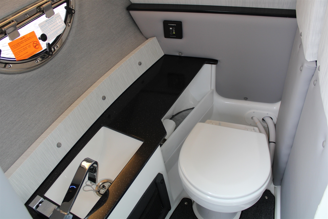 Compact boat bathroom featuring a toilet, sink with faucet, and window with safety notices. Modern design and functionality.